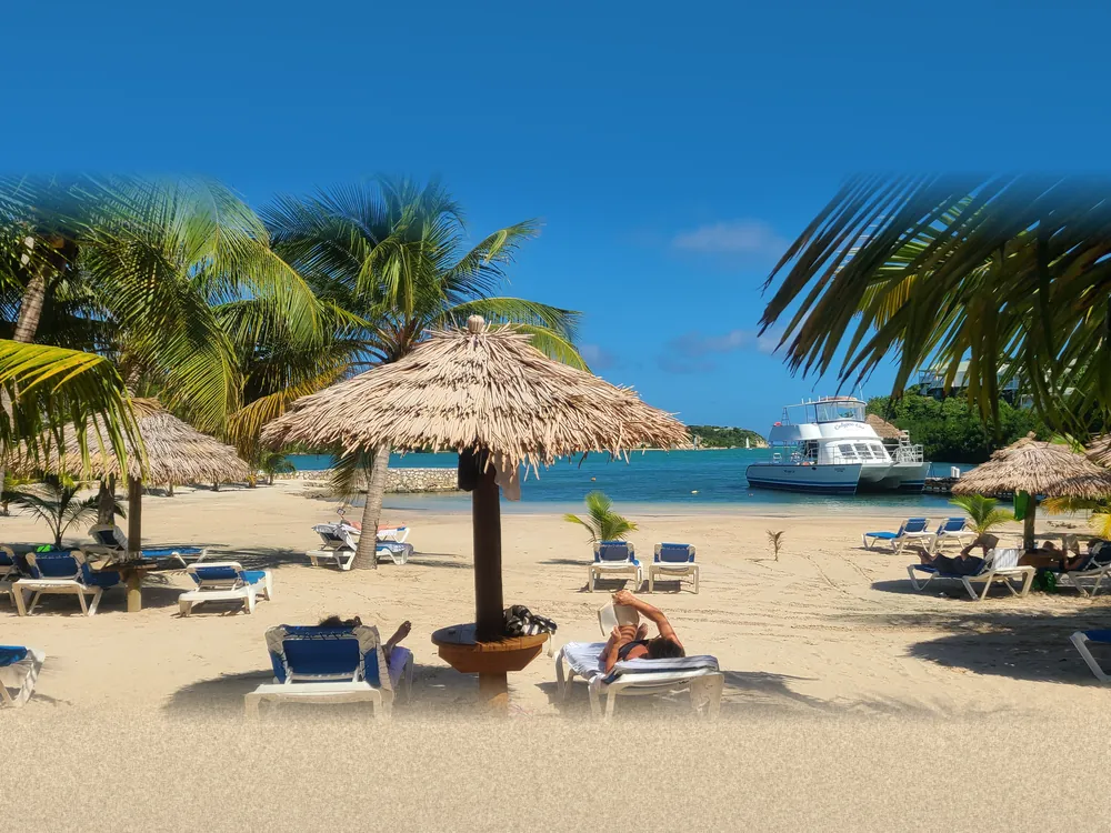 A thatched palapa umbrella and loungers on a white sand beach at a Caribbean resort, with turquoise water beyond